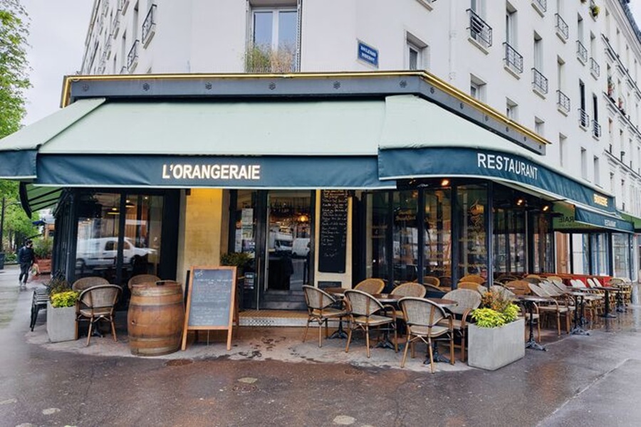 Corner bistro with green awning and wicker outdoor seating on wet pavement.