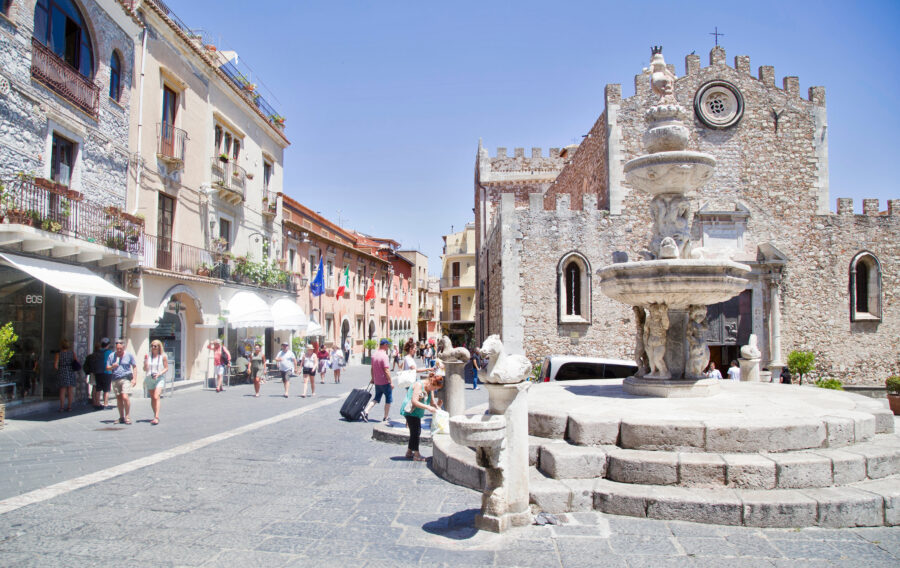 Corso Umberto I in Taormina, Sicily, featuring a decorative fountain surrounded by historic buildings and vibrant street life