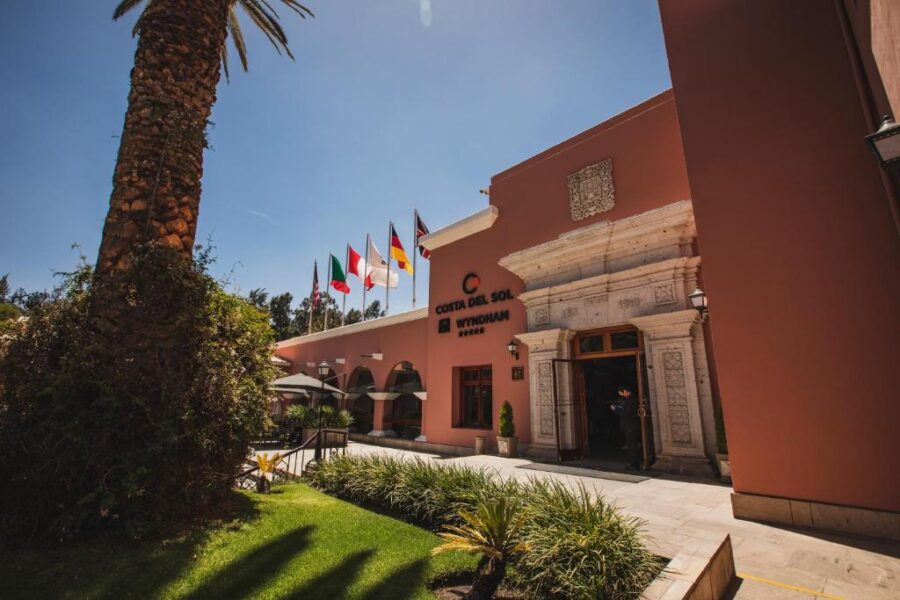 Wyndham Costa del Sol Arequipa hotel exterior with palm tree, terrace, flags and sunny courtyard.