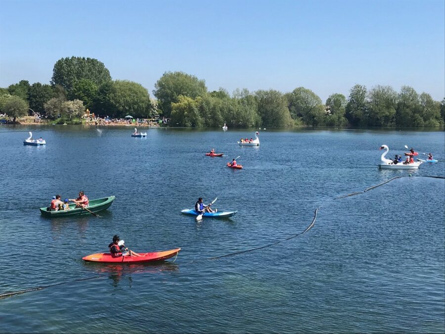 Several kayakers enjoying a sunny day on the lake at Cotswold Water Park & Beach, with trees in the background.