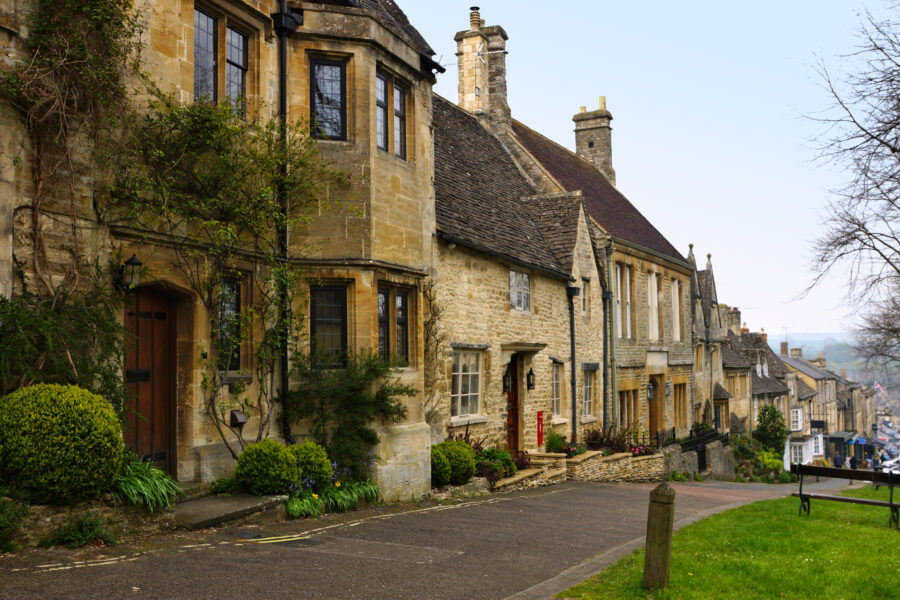 Charming stone houses line a picturesque street in the Cotswolds village of Burford, England, showcasing traditional architecture.