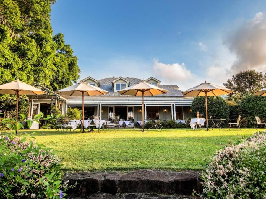Luxury countryside inn garden restaurant with outdoor terrace dining, umbrellas, manicured lawn, and trees.