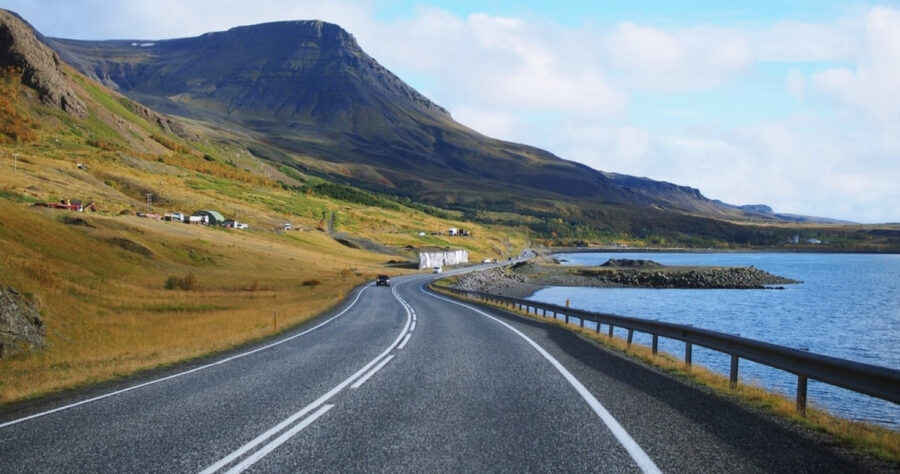 Scenic winding road through Icelandic countryside with mountains, lake, and autumn foliage.