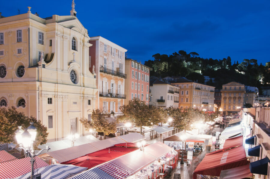 Cours Saleya in Nice, France, illuminated at night, showcasing vibrant market stalls and lively outdoor dining.