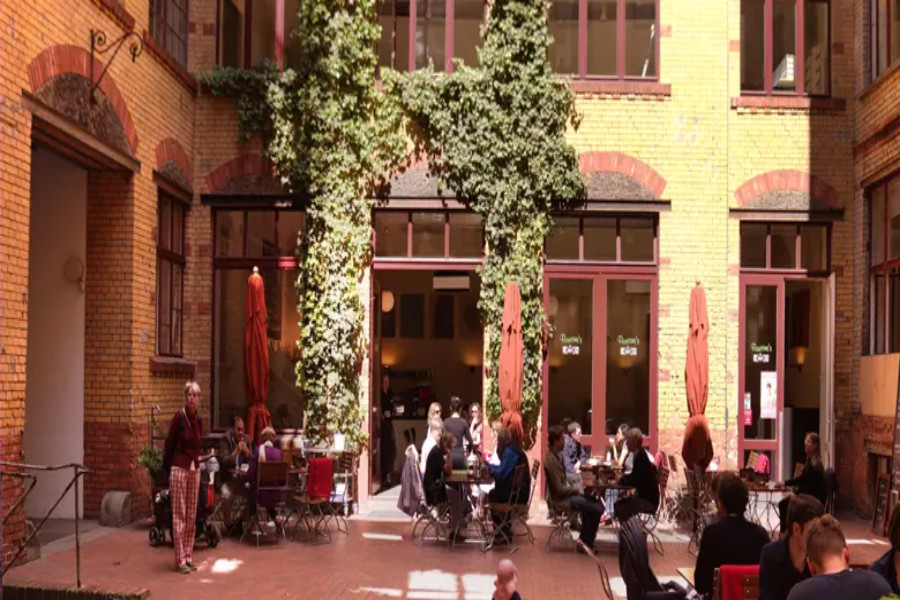 Sunlit courtyard cafe with outdoor seating and ivy-covered brick facade.
