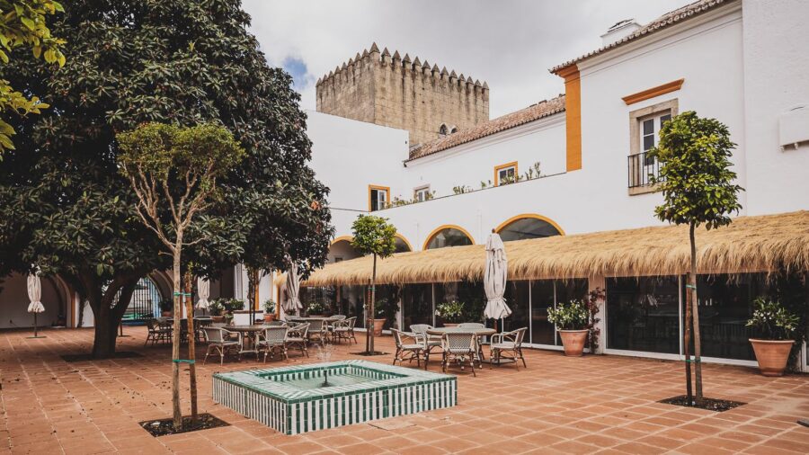 Historic courtyard with fountain, modern seating, and castle backdrop under soft light.