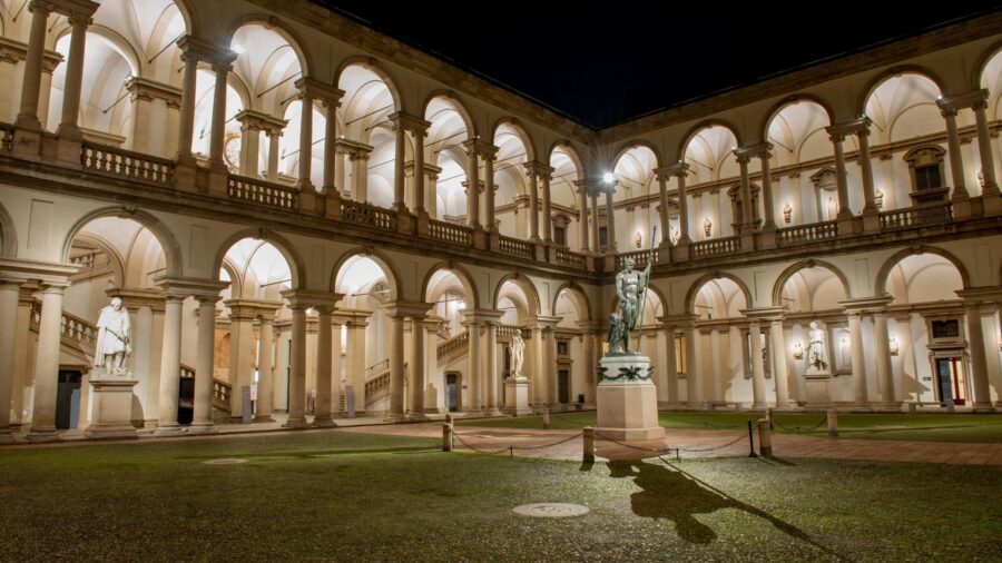 Elegant historical courtyard at night with statues, arches, and dramatic lighting.