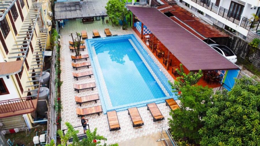 Aerial view of SaBai Backpacker Hostel courtyard pool with sun loungers, terrace dining, tropical plants.