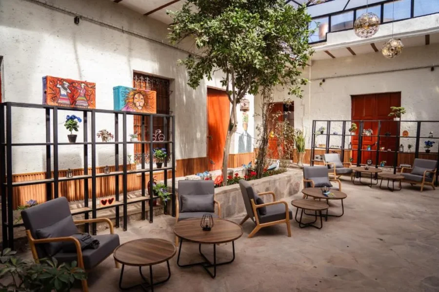 Modern courtyard lounge with tree, outdoor café seating, cozy chairs, and artistic wall decor.