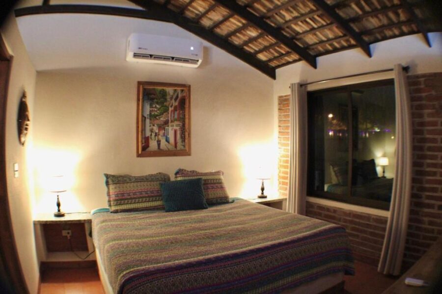 Cozy rustic bedroom with striped bedding, brick wall, wooden ceiling beams, and window at night.