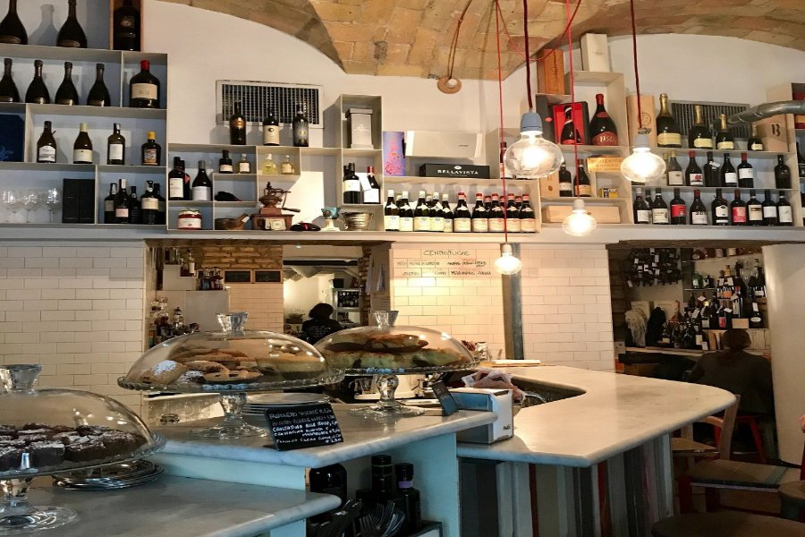 Cozy marble bar wine cafe with pastries under glass domes and exposed brick wine shelves.