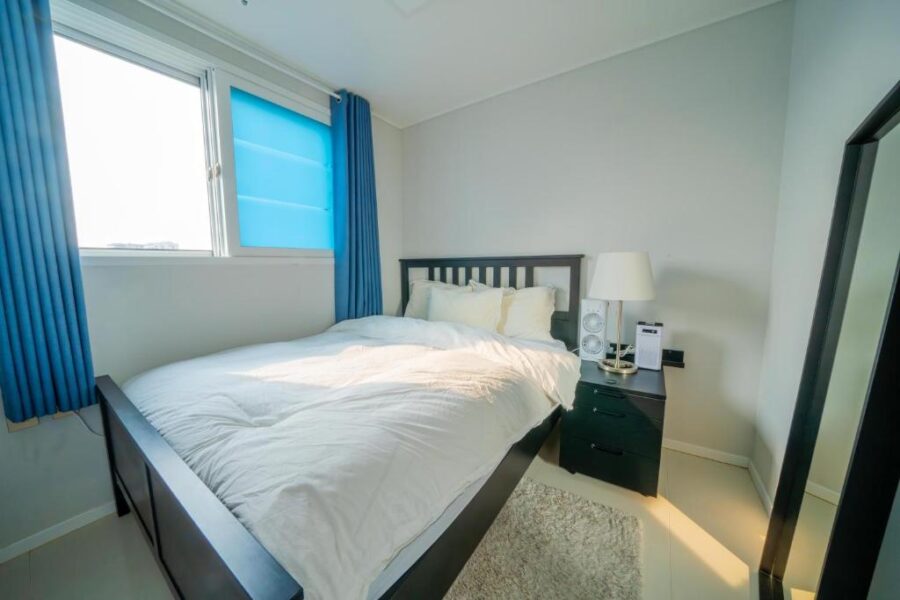Cozy modern bedroom with natural light, white duvet, blue curtains, and dark wooden accents.