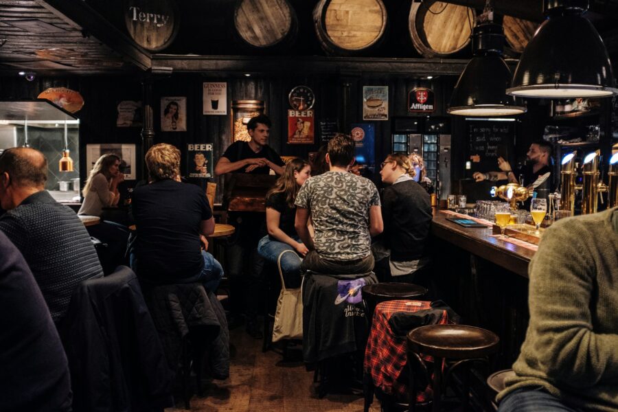 Cozy Veliko Tarnovo pub interior with patrons, wooden bar, beer taps, and warm lighting.