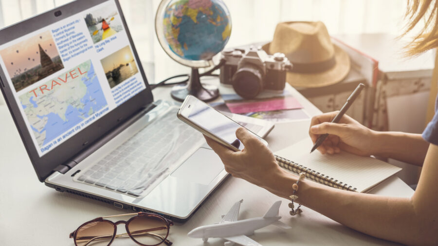 Travel workspace with laptop, globe, camera, and sunhat evoking adventure and planning.