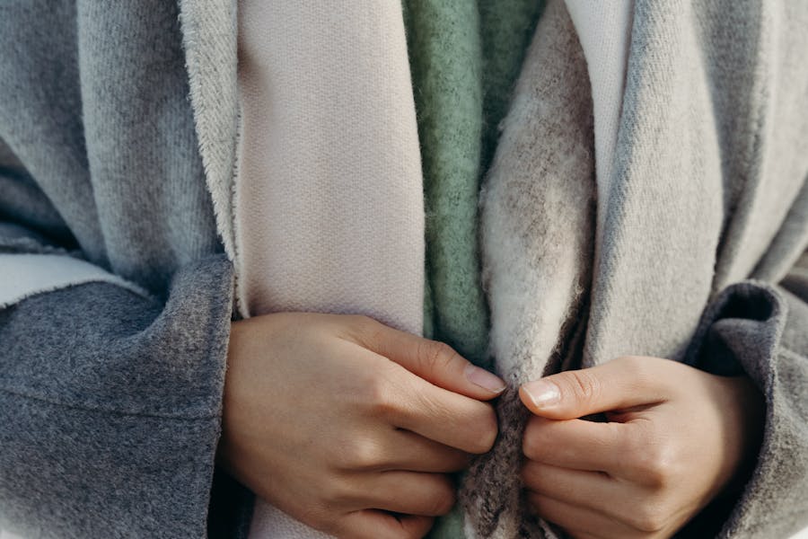 Cozy winter layers closeup of hands holding warm textured coat and soft neutral fabrics.