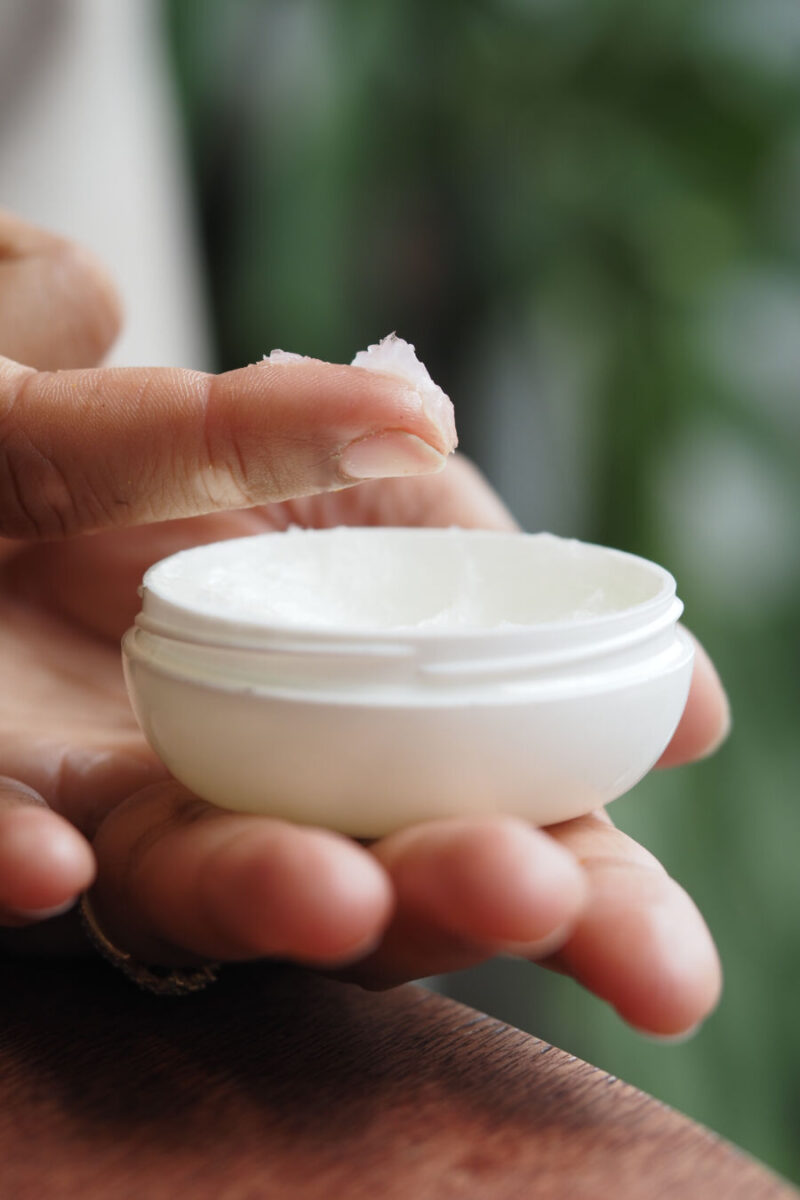 Hand applying petroleum jelly from a white container in a well-lit indoor space.