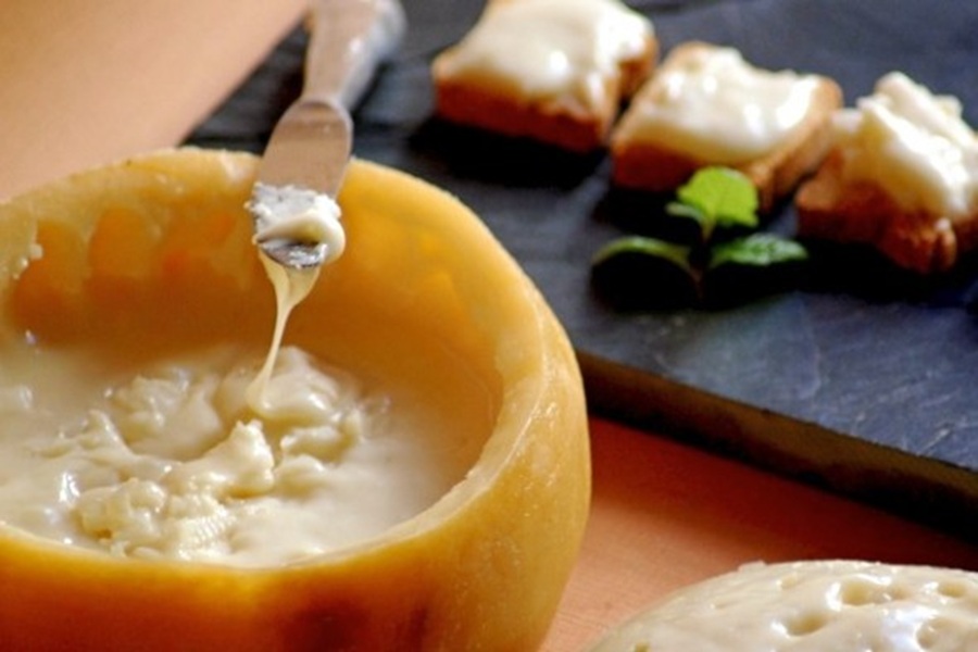Melted cheese in rind with bread and mint on a slate board.