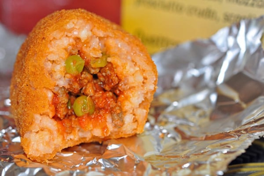 Golden-brown arancini with savory meat, peas, and tomato filling on shiny foil.