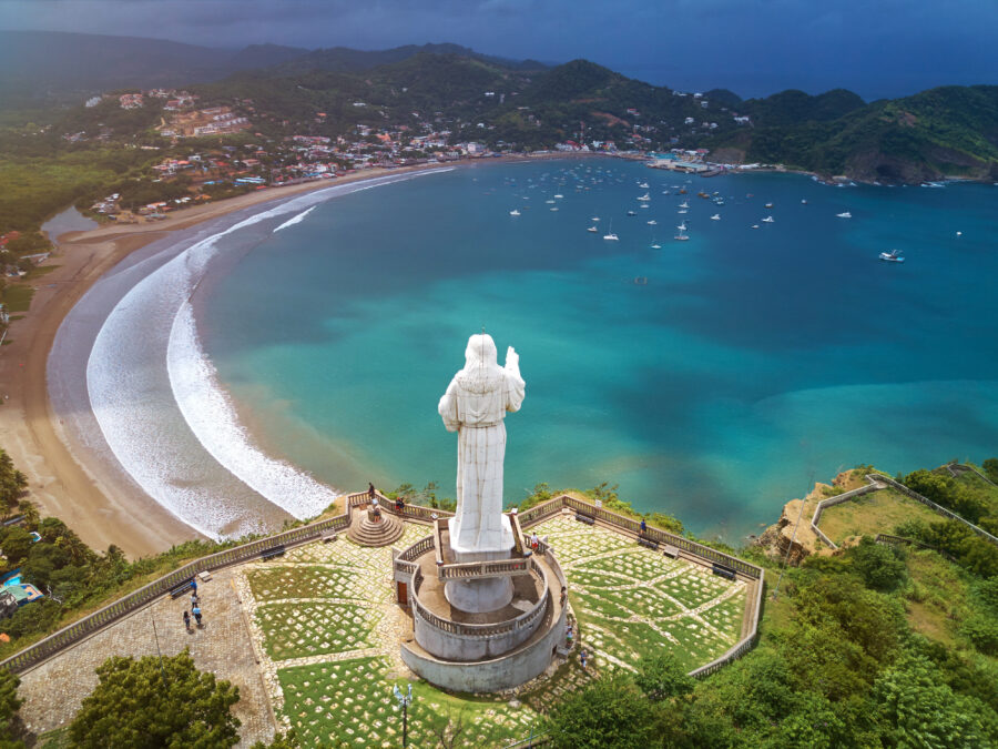 Panoramic view of Cristo de la Misericordia statue overlooking San Juan Del Sur, with lush hills and ocean in the background