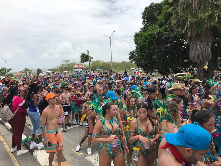 Vibrant group of people in colorful costumes celebrating the Crop Over Festival on a lively street in Barbados.