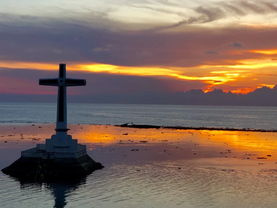 Cross at sunset over tidal seascape with water reflection.