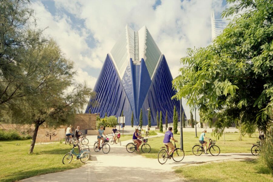 Modern urban park scene with cyclists, greenery, and striking blue glass architecture.