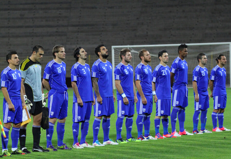 Cyprus National Football Team players celebrating a goal on the field, wearing red and white uniforms.
