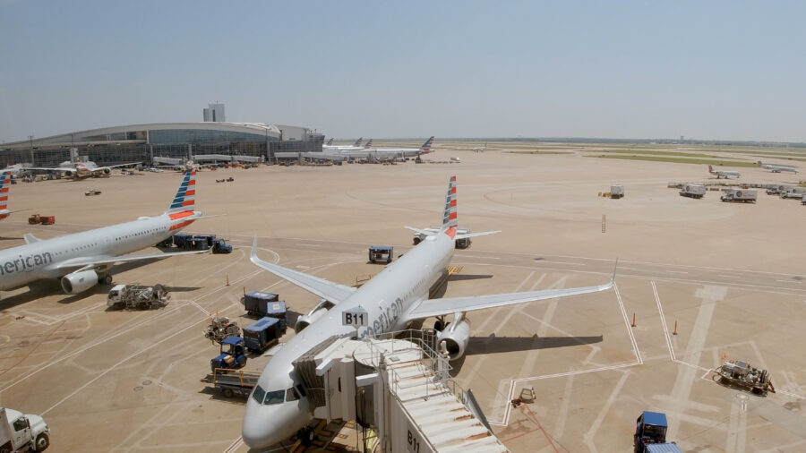  Several American Airlines aircraft lined up on the tarmac at Dallas Fort Worth Airport, with terminal buildings in the background