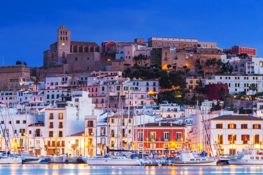 Night view of Ibiza Dalt Vila with illuminated buildings reflecting in the water, showcasing the vibrant atmosphere of Ibiza, Spain
