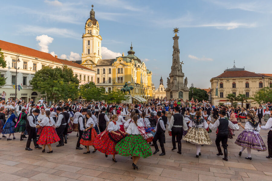 Folk dancers in traditional costumes performing in a historic European square during a cultural festival.