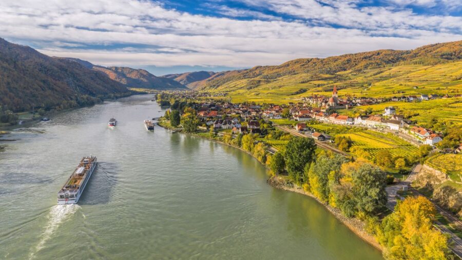 Picturesque Danube river landscape with vineyards, villages, and riverboats, showcasing serene autumn beauty.