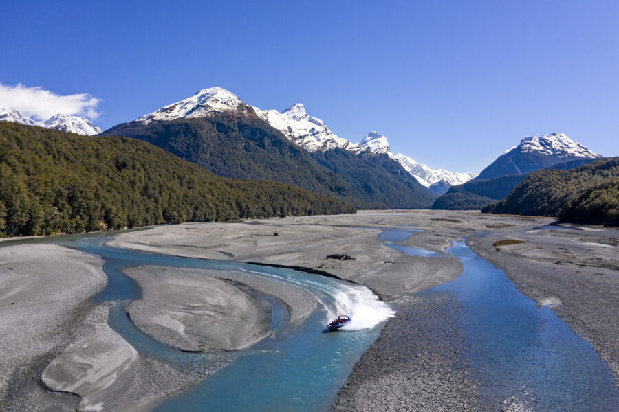 Jet boat on Dart River in Glenorchy New Zealand with braided riverbed and snowy mountains.