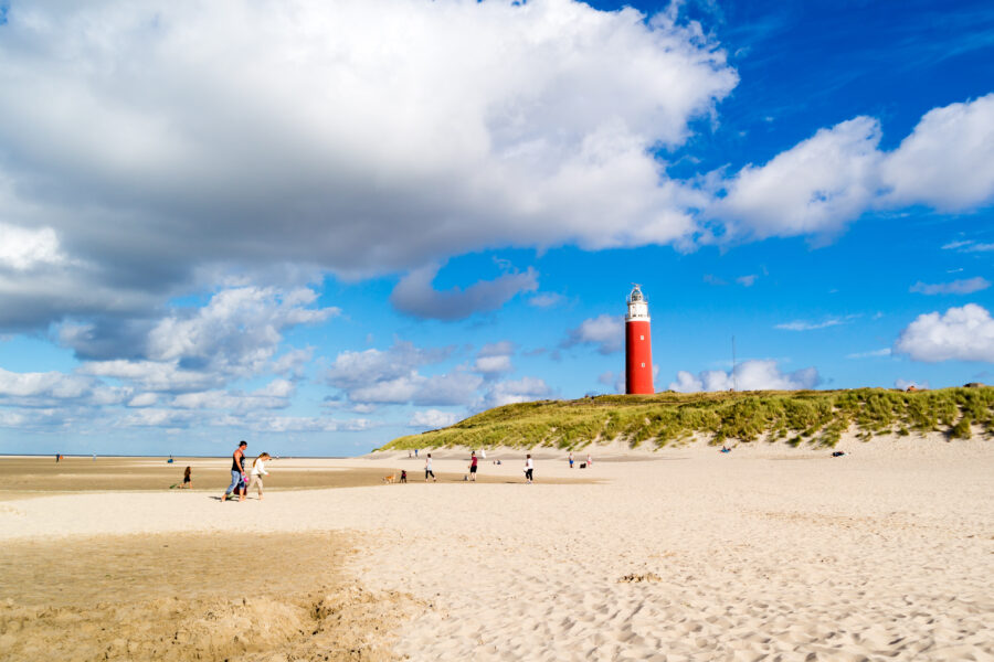 Scenic view of De Cocksdorp beach and lighthouse on Texel Island, Netherlands, featuring golden sand and ocean waves.