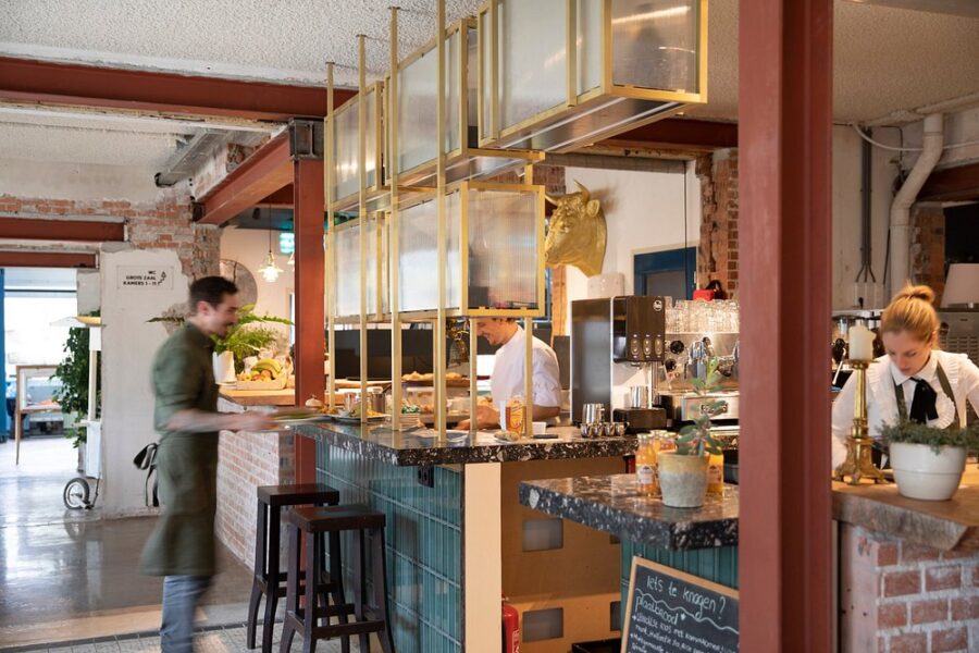 Busy restaurant, De Groene Afslag Amsterdam, with staff working at the counter and customers in the background.