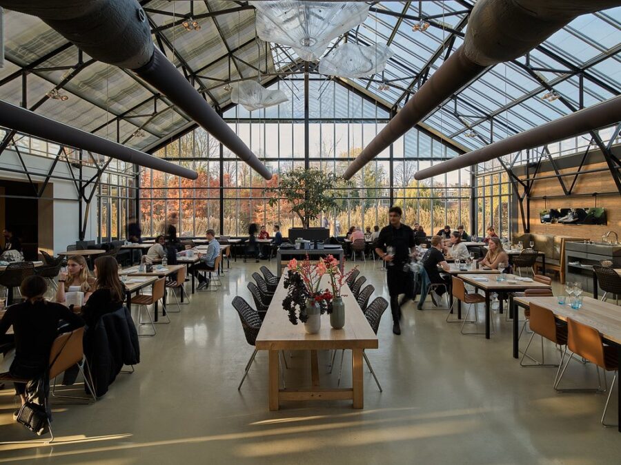 Interior of De Kas greenhouse in Amsterdam, featuring tables and chairs among lush greenery.