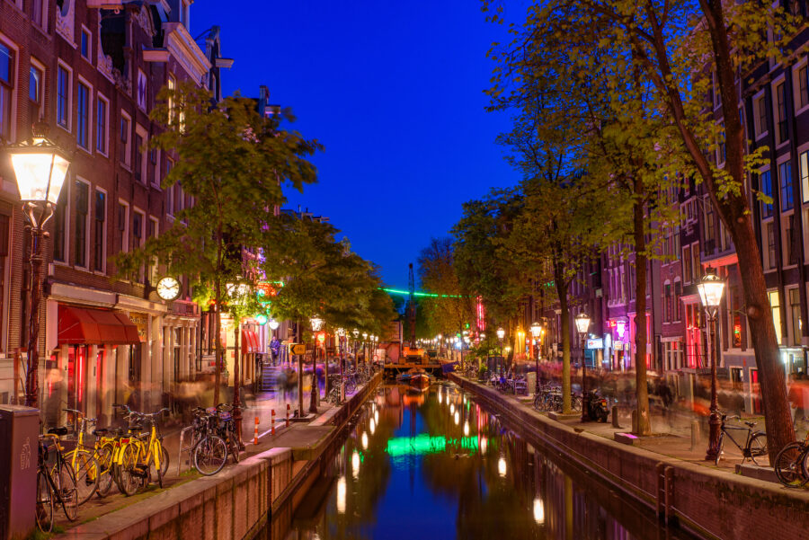 Night view of De Wallen, Amsterdam's red-light district, showcasing illuminated windows and bustling streets.