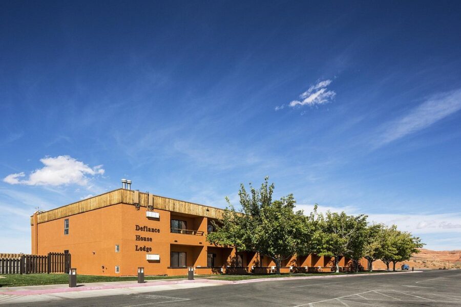 Exterior view of Defiance House Lodge in Utah, featuring a motel building and a spacious parking lot.
