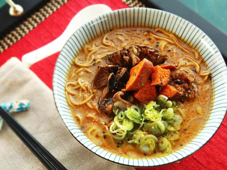 Vegan ramen with vibrant toppings, savory broth, and noodles in a striped blue and white bowl.