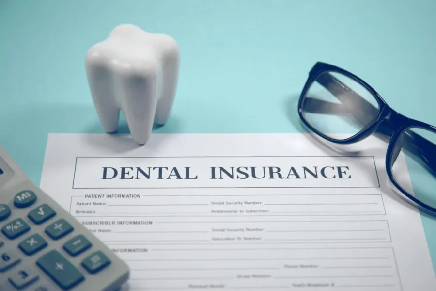 Dental insurance document with tooth figurine, calculator, and glasses on a desk.