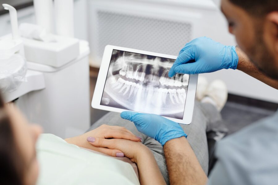 Dentist explaining X-ray on tablet to patient in modern dental office.