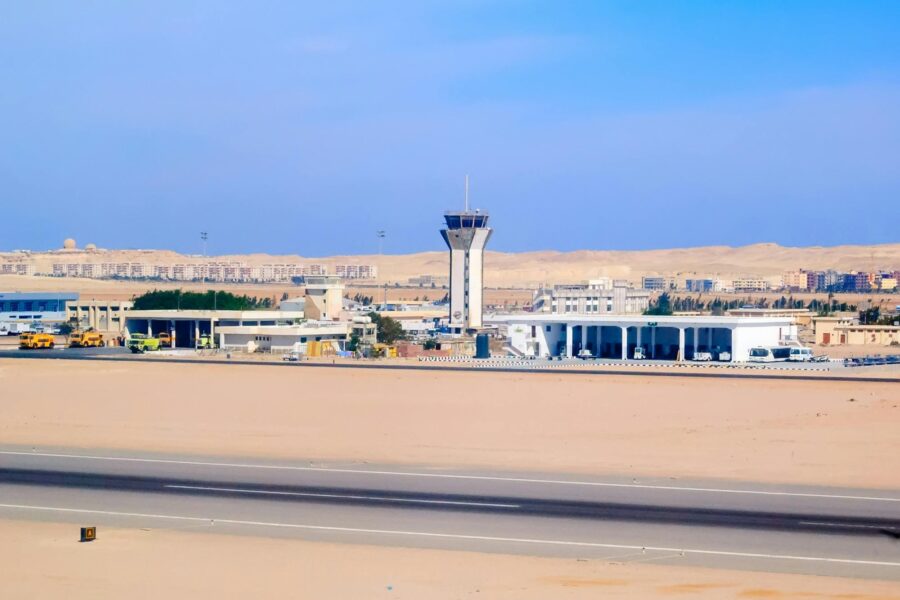 Hurghada International Airport runway with control tower, terminal buildings and desert city skyline in background.