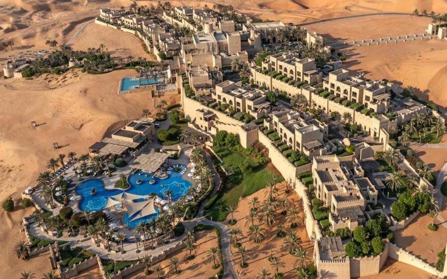 Luxury desert resort oasis with citadel-style architecture, infinity pool, palm trees, and golden sand dunes.