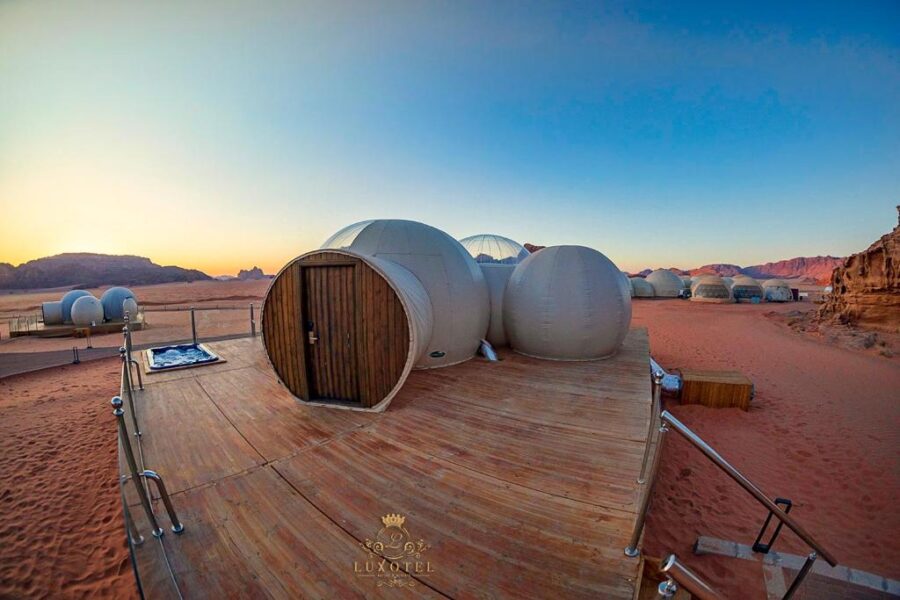 Luxury Wadi Rum desert glamping domes at sunset on wooden platforms with rocky mountains.
