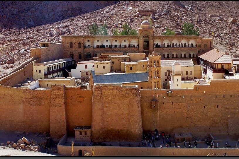 St. Catherine’s Monastery fortress in Sinai desert with stone walls, church bell tower, and mountains.