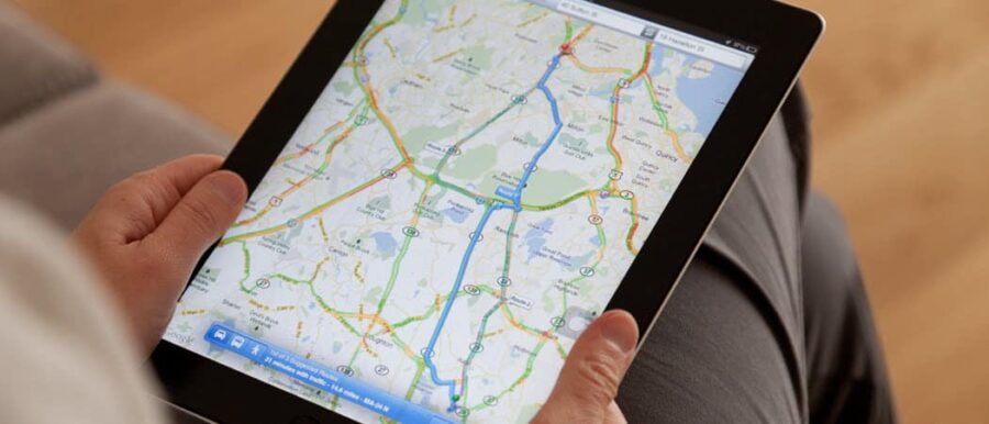 Close-up of a hand holding a tablet displaying a digital navigation map with traffic colors.