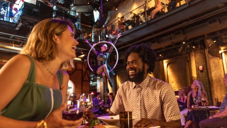 Dining and entertainment at lively restaurant with acrobat, joyful patrons, and vibrant atmosphere.