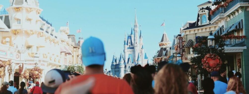 Theme park crowd approaches iconic Disneyland castle on a sunny autumn day.