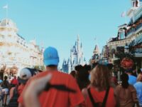 Theme park crowd approaches iconic Disneyland castle on a sunny autumn day.