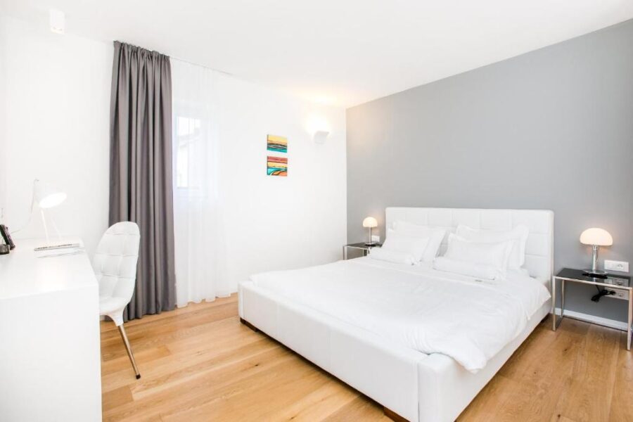 Bright bedroom with a white bed and wooden flooring, located in Divota Apartment Hotel, Split, Croatia.