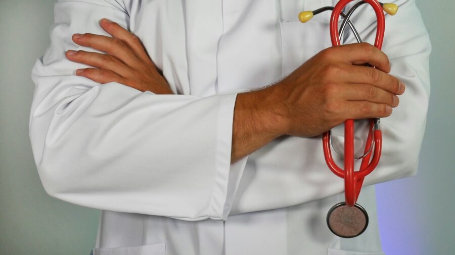 Doctor in white coat holding red stethoscope, representing professionalism and healthcare expertise.